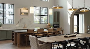 A modern kitchen with a large island, wooden chairs, pendant lighting, and a view of the outside. - Landing | Chic 1BD in Lochridge (Cary)