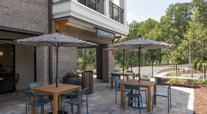 An outdoor seating area with tables and chairs, umbrellas, and a sign that reads 'TRAPEZE'. - Landing | Amazing 1BD in Lochridge (Cary)