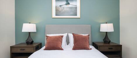 A neatly made bed with two pillows, a headboard, and two bedside tables with lamps.