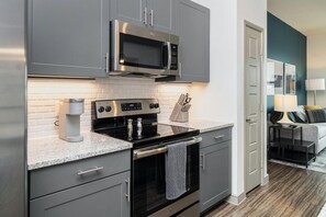 A modern kitchen with grey cabinetry, a built-in microwave, a stove, and a coffee maker. - Landing | Amazing 1BD in Lochridge (Cary)