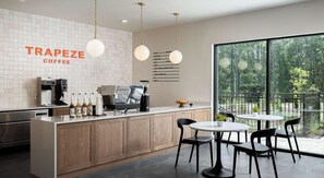 A modern coffee shop interior with a barista station, seating area, and large windows overlooking a forest. - Landing | Modern 1BD in Lochridge (Cary)