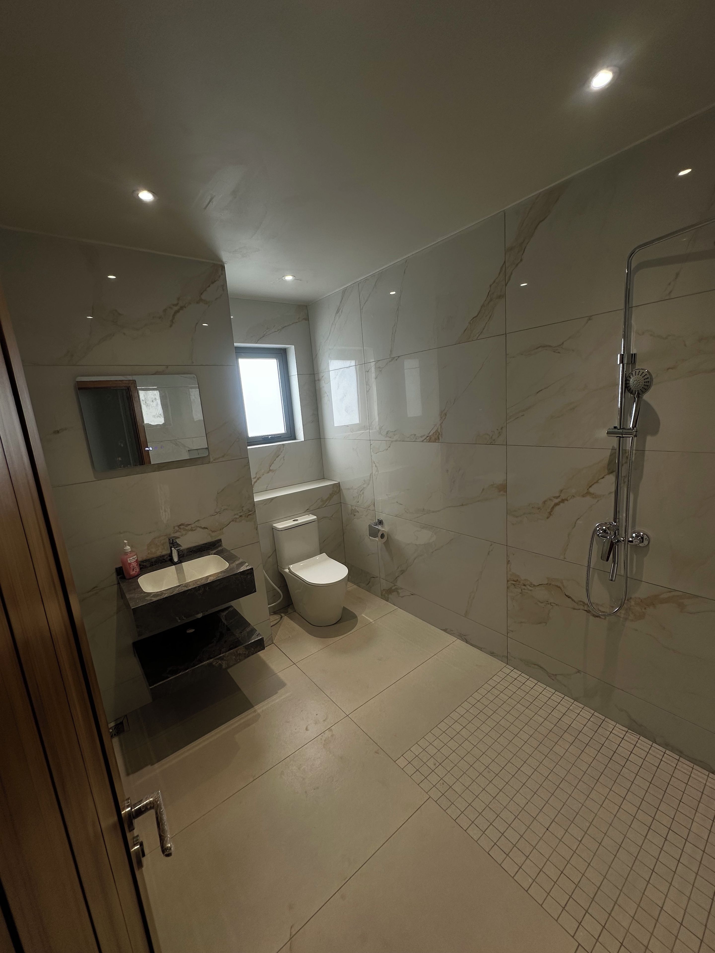 Une salle de bain moderne avec un sol en marbre, des toilettes, un lavabo, un miroir et une douche.