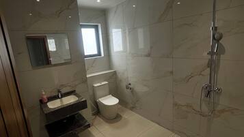A modern bathroom with a marble floor, a toilet, a sink, a mirror, and a shower.