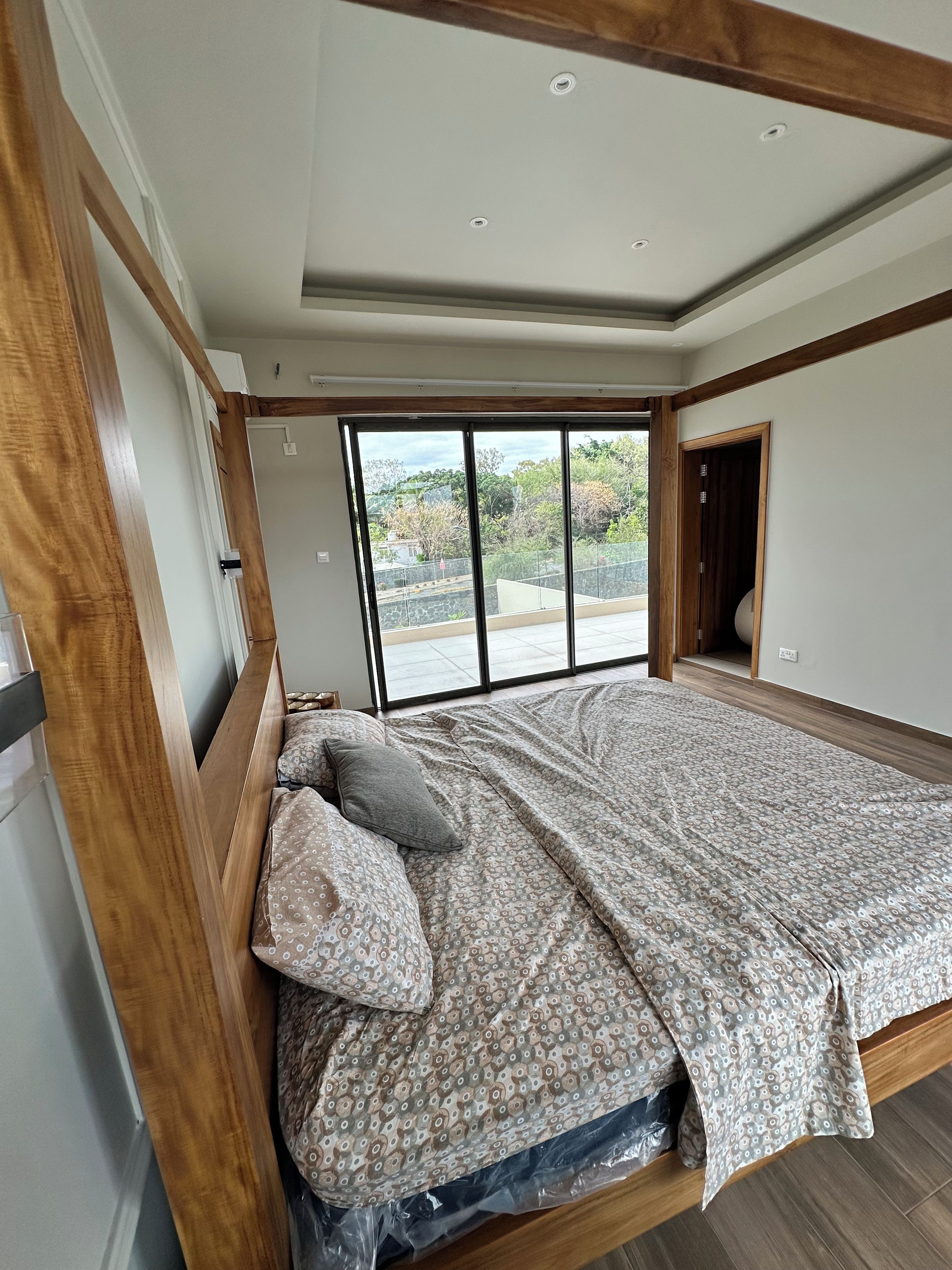 Una camera da letto con una grande finestra, un letto con lenzuola fantasia e travi in legno al soffitto.