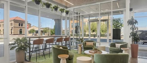 A modern indoor space with large windows, green upholstered seating, and potted plants.