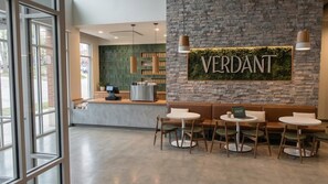 A reception area with a stone wall, a mounted sign reading 'VERDANT,' and a seating area with round tables and chairs. - Landing | Beautiful 1BD in West Side (Grand Rapids)