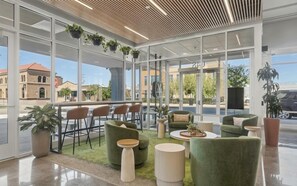 A modern indoor space with large windows, green upholstered seating, and potted plants. - Landing | Beautiful 1BD in West Side (Grand Rapids)