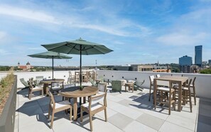 Terraço no topo com área de estar externa, incluindo mesas e cadeiras, e um grande guarda-sol para proteção contra o sol.