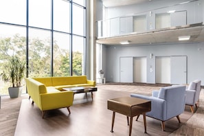 Un hall d’entrée spacieux avec un canapé jaune, une table basse en bois et un fauteuil gris.
