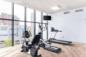A gym with cardio machines, a TV, and large windows with a city view. - Landing | Stylish 1BD in University Circle (Cleveland)