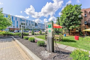 A parking area with electric vehicle charging stations, a paved walkway, and a building with multiple windows in the background. - Landing | Beautiful 1BD in University Circle (Cleveland)