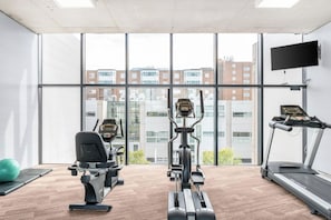 Ein Fitnessraum mit Cardiogeräten, Laufband und einem großen Fenster mit Blick auf die Stadt.
