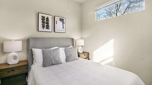 A bedroom with a bed, two bedside tables, a window, and two framed pictures on the wall. - Landing | Beautiful 2BD in Central West End (St. Louis)