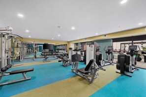 Ein Fitnessraum mit unterschiedlichen Trainingsgeräten, einer Spiegelwand und einem Poolbereich.