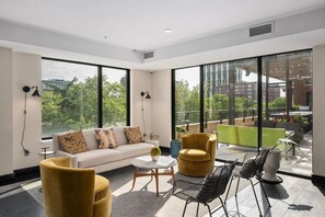 A modern living room with a sofa, armchairs, a coffee table, and a dining area with chairs. Large windows provide a view of the cityscape. - Landing | Chic 2BD in Central West End (St. Louis)
