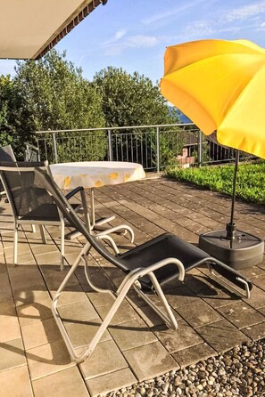 An outdoor patio with a table and chairs, a yellow umbrella, and a metal fence. - Bee Aeschi by Interhome (Aeschi bei Spiez)