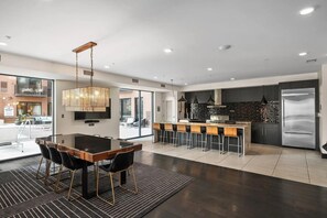 A modern kitchen with a stainless steel refrigerator, a bar area, and a dining space with a large table and chairs. - Landing | Incredible 2BD in Central West End (St. Louis)