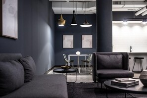 A modern living room with dark walls, a sofa, a coffee table, and a dining area with chairs and a table. - Landing | Spectacular 1BD, Yoga Studio (Akron)
