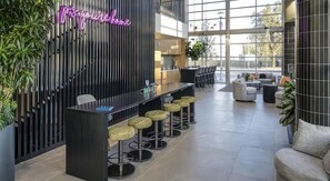 Un'area bar moderna con insegna al neon, sgabelli alti e un angolo salotto con divano e tavolino.