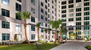 A modern building with multiple floors, large windows, and a well-maintained outdoor area with palm trees and a hammock. - Landing | Incredible Studio, Clubhouse, Gym (Orlando)