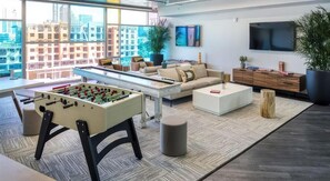 A modern living room with a foosball table, a sofa, a coffee table, and a TV. - Landing | Amazing Studio, Gym, Courtyard (Orlando)