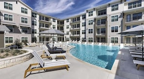 A multi-story residential building with a swimming pool, outdoor seating, and a clear sky. - Landing | Chic 2BD in Downtown Dripping Springs (Dripping Springs)