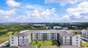 Un edificio residencial de varios pisos con un patio central, rodeado de vegetación y un cielo despejado.