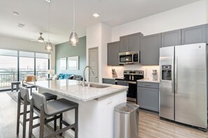 A modern kitchen with a central island, stainless steel appliances, and a large window offering a city view. - Landing | Stylish 2BD in Downtown Dripping Springs (Dripping Springs)