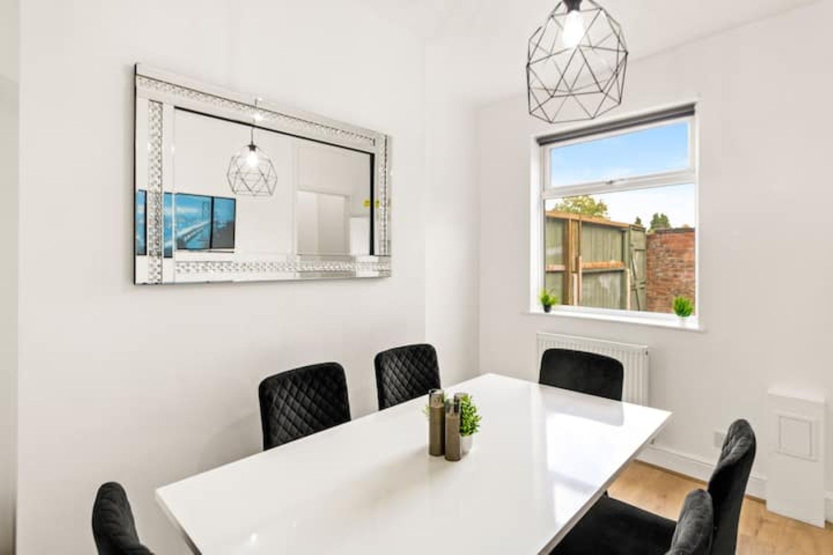 Une salle à manger moderne avec une table blanche, des chaises noires, un miroir décoratif et un luminaire suspendu.