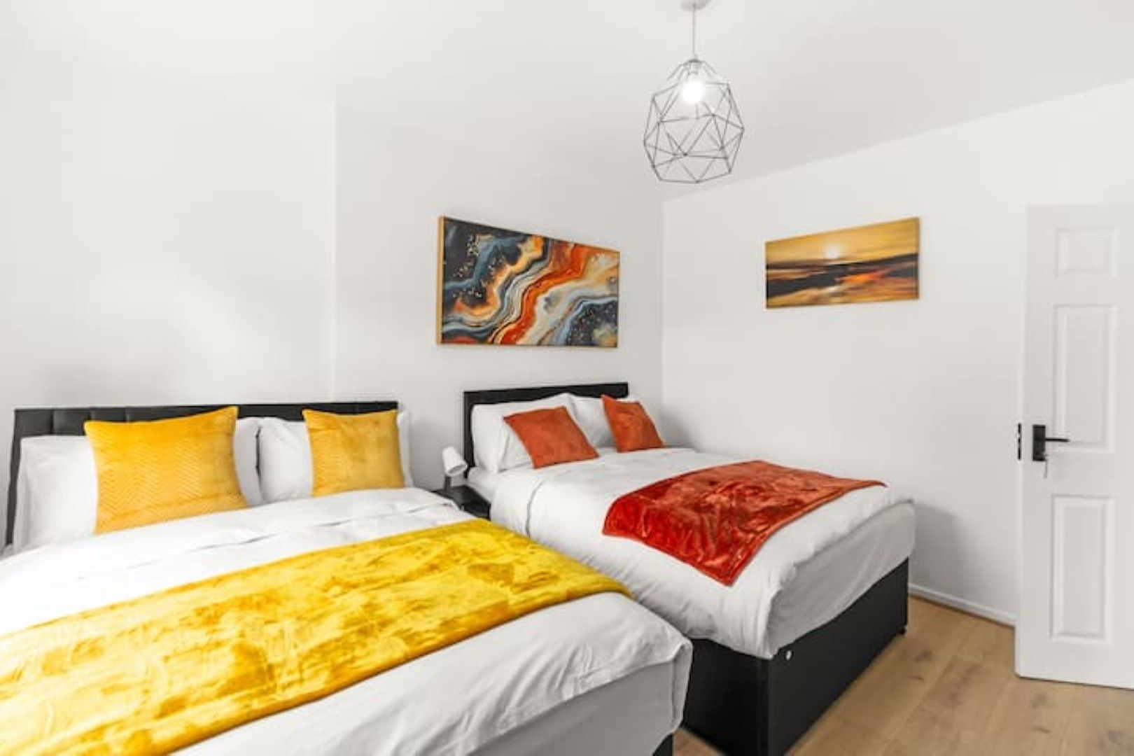 Une chambre d’hôtel avec deux lits, des murs blancs et des œuvres d’art accrochées aux murs.
