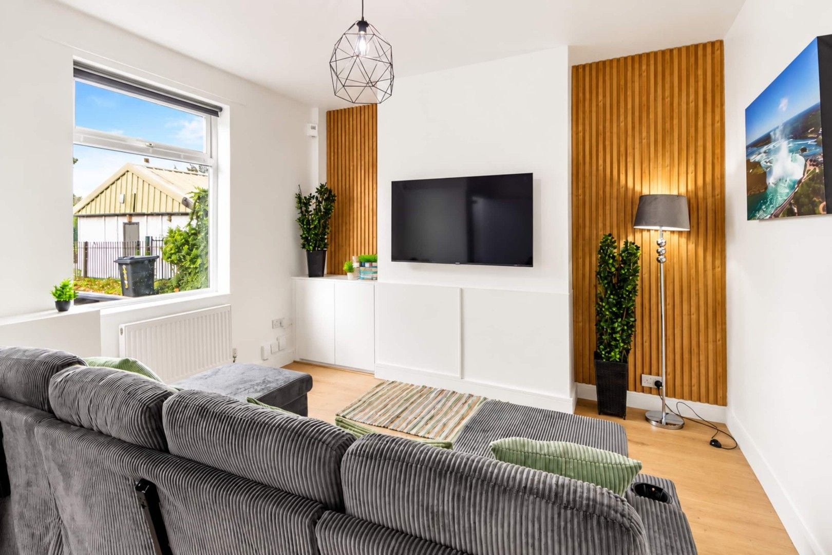 A modern living room with a sectional sofa, a flat-screen TV, wooden paneling, and a view of the outdoors.