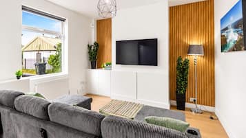 A modern living room with a sectional sofa, a flat-screen TV, wooden paneling, and a view of the outdoors.