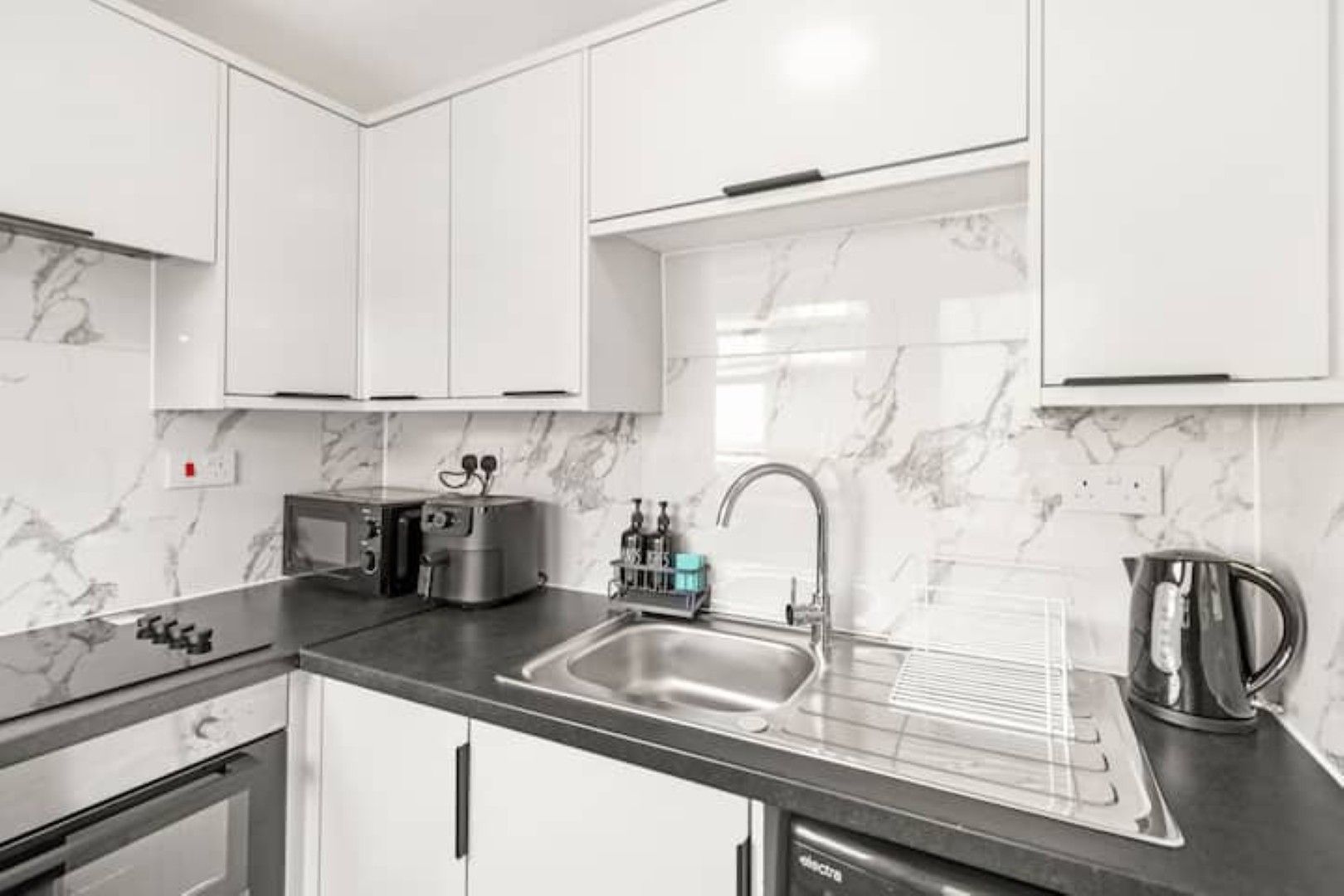 A modern kitchen with white cabinets, a stainless steel sink, a kettle, and a toaster.