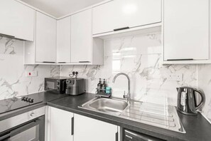 Een moderne keuken met witte kastjes, een roestvrijstalen spoelbak, een waterkoker en een broodrooster.