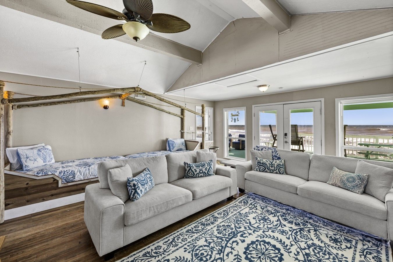 A spacious living area with a high ceiling, a ceiling fan, and a view of the beach through large windows.