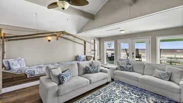 A spacious living area with a high ceiling, a ceiling fan, and a view of the beach through large windows.