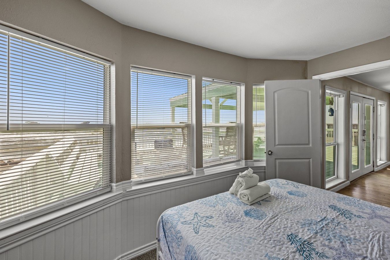A bedroom with a bed, a window with blinds, a door, and a view of the outside.