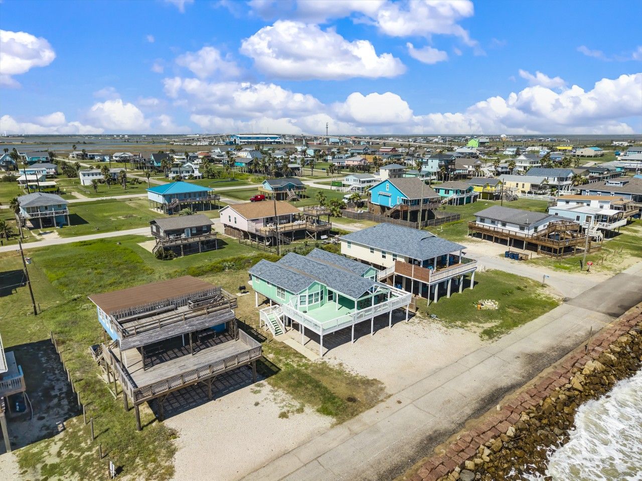 A coastal residential area with houses, some with waterfront views, and a beach in the foreground.