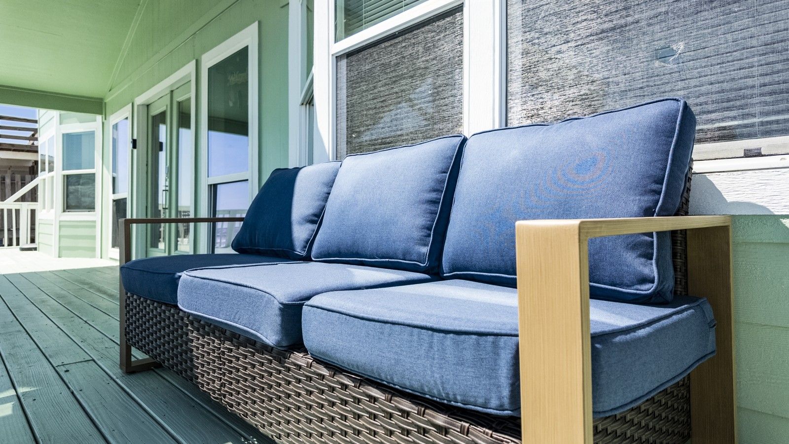 A wicker sofa with cushions on an outdoor deck.