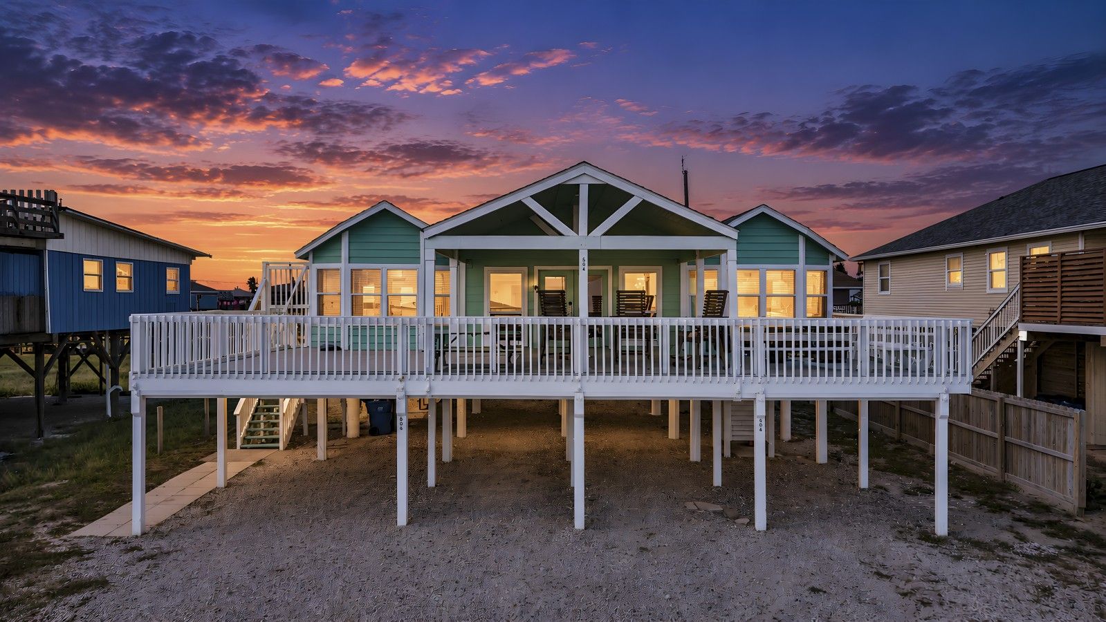 A waterfront property with a covered deck, multiple buildings, and a sunset sky.