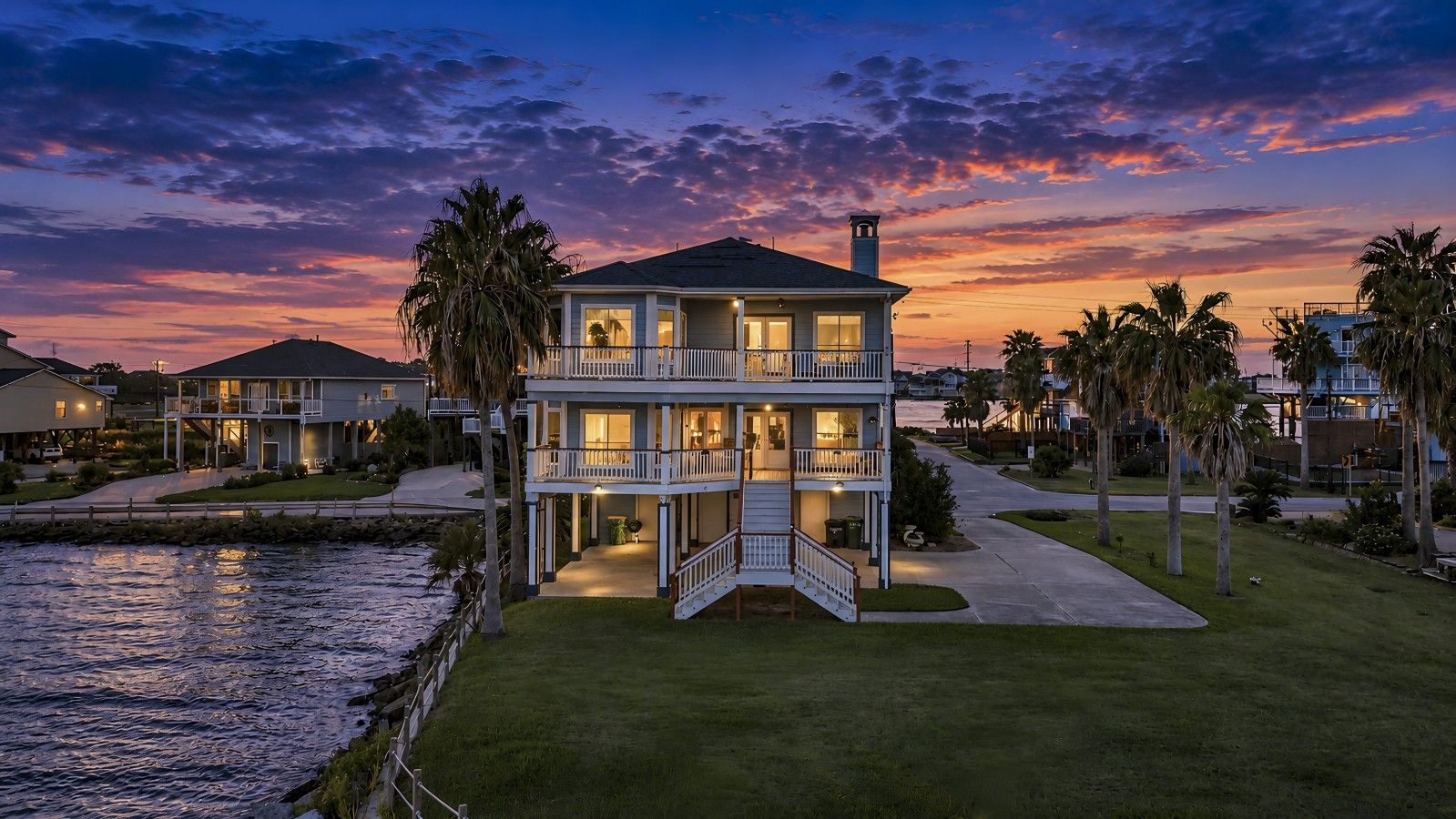 A two-story waterfront property with a balcony, a staircase leading to the entrance, and a view of the water.