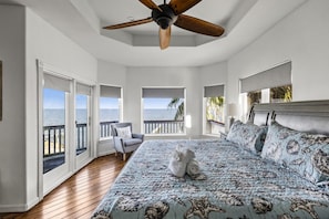 A bedroom with a large bed, a ceiling fan, and a view of the ocean through multiple windows. - Far Harbor- Waterfront | Close to Kemah Boardwalk (Kemah Area)