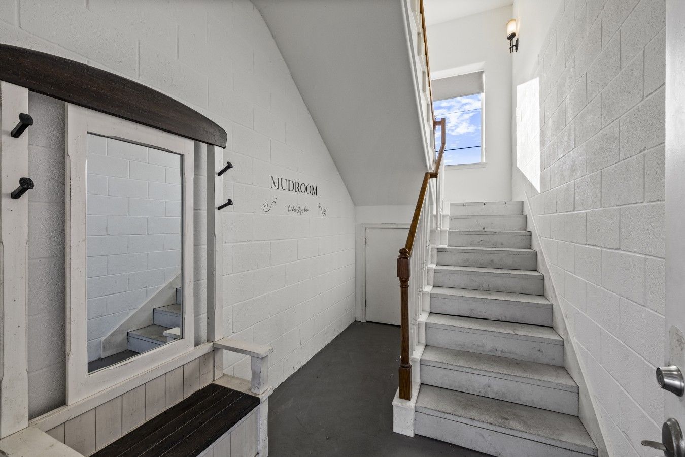 Una escalera con paredes de ladrillo blanco y barandilla de madera que conduce a una puerta con la leyenda 'MUDROOM'.