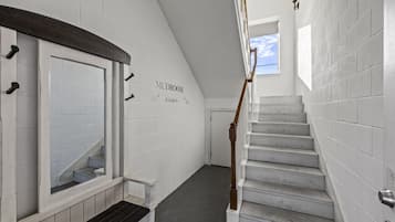 Una escalera con paredes de ladrillo blanco y barandilla de madera que conduce a una puerta con la leyenda 'MUDROOM'.
