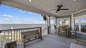 A covered outdoor deck with a bench, table, chairs, and a ceiling fan.