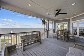 A covered outdoor deck with a bench, table, chairs, and a ceiling fan. - Far Harbor- Waterfront | Close to Kemah Boardwalk (Kemah Area)