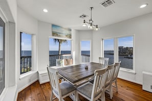 A dining area with a wooden table and chairs, large windows with a view of the water, and a ceiling light fixture. - Far Harbor- Waterfront | Close to Kemah Boardwalk (Kemah Area)