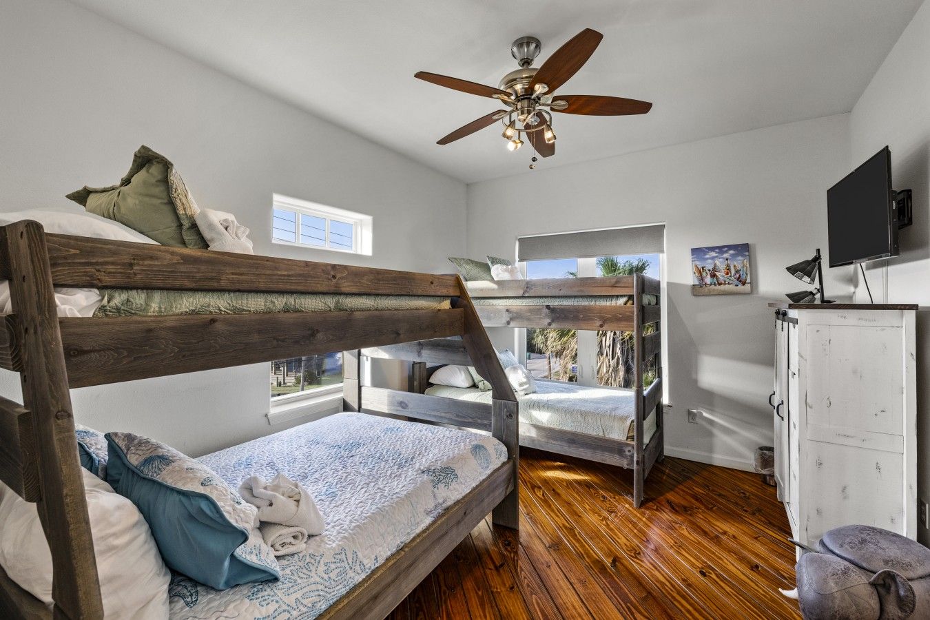 Ein Schlafzimmer mit Etagenbetten, einem Deckenventilator, Holzboden, einem weißen Kleiderschrank und einem Fenster mit Blick.