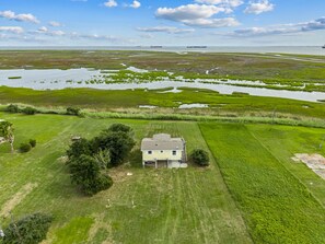 A single-story house with a front porch, surrounded by a well-maintained lawn and a marshy area with water channels. - Warblers Roost- Bird Watcher Paradise | Great view (Crystal Beach)