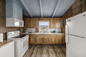 A kitchen with wooden cabinets, a white refrigerator, a stove, a microwave, and a window with a view. - Warblers Roost- Bird Watcher Paradise | Great view (Crystal Beach)